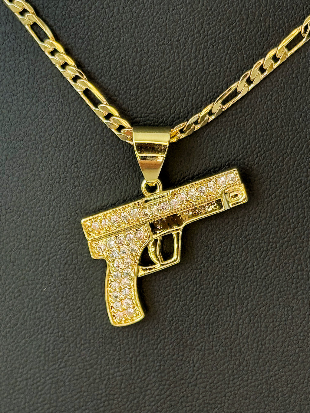 Gold gun-shaped pendant on a chain against a dark background