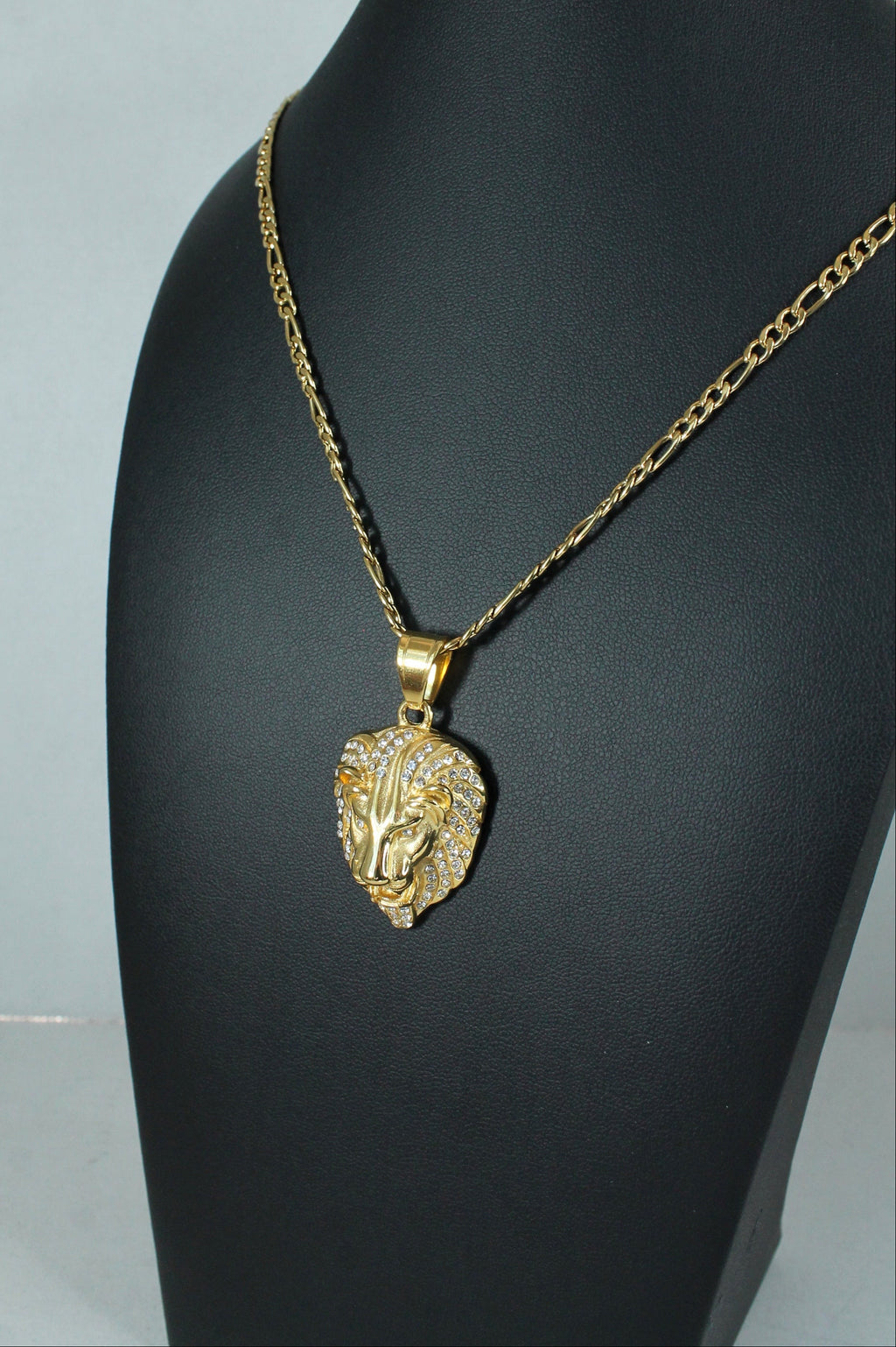 A gold chain necklace with a textured lion head pendant, displayed on a black mannequin bust against a light gray background.