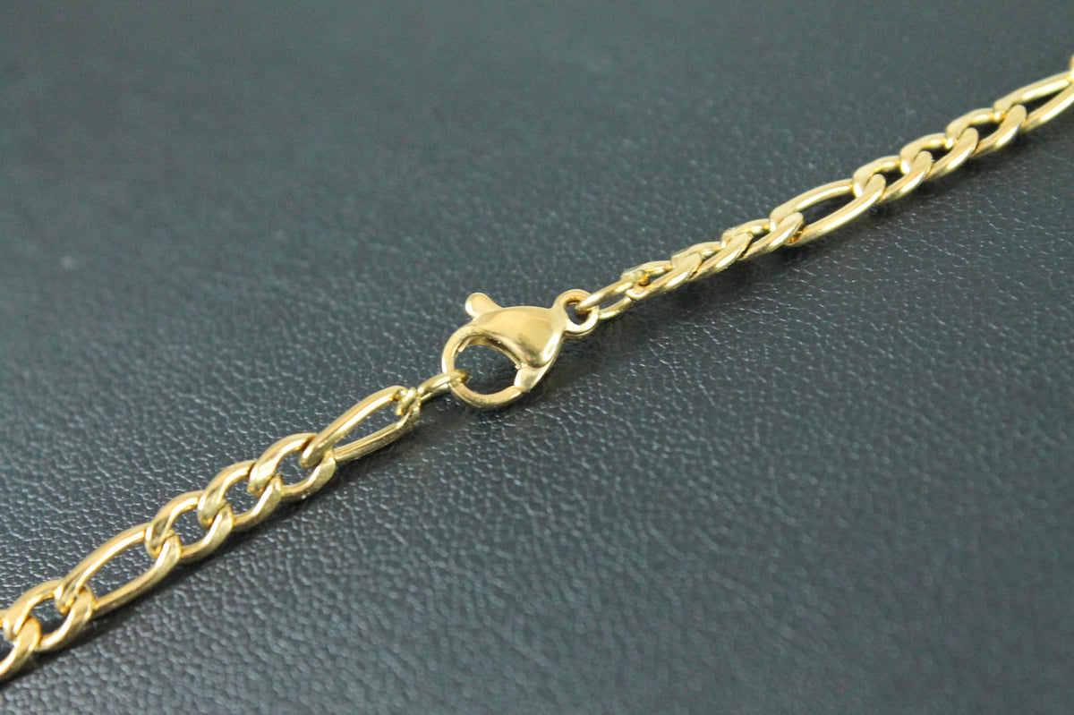 A close-up of a gold chain necklace with a lobster clasp, resting on a dark textured surface.