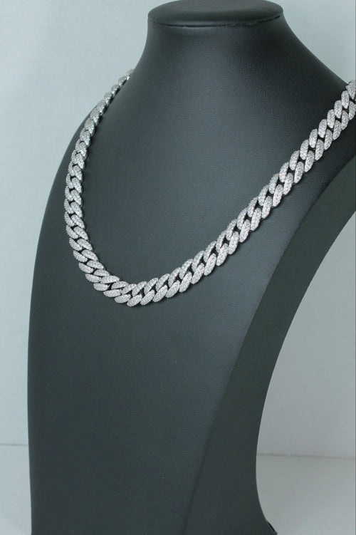 A silver-toned Cuban link chain necklace displayed on a matte black jewelry bust against a light gray background.