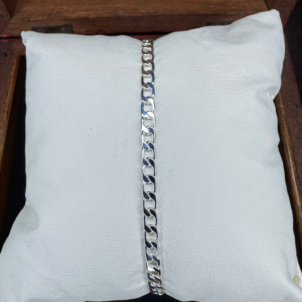 Silver chain bracelet on a white cushion with a wooden background