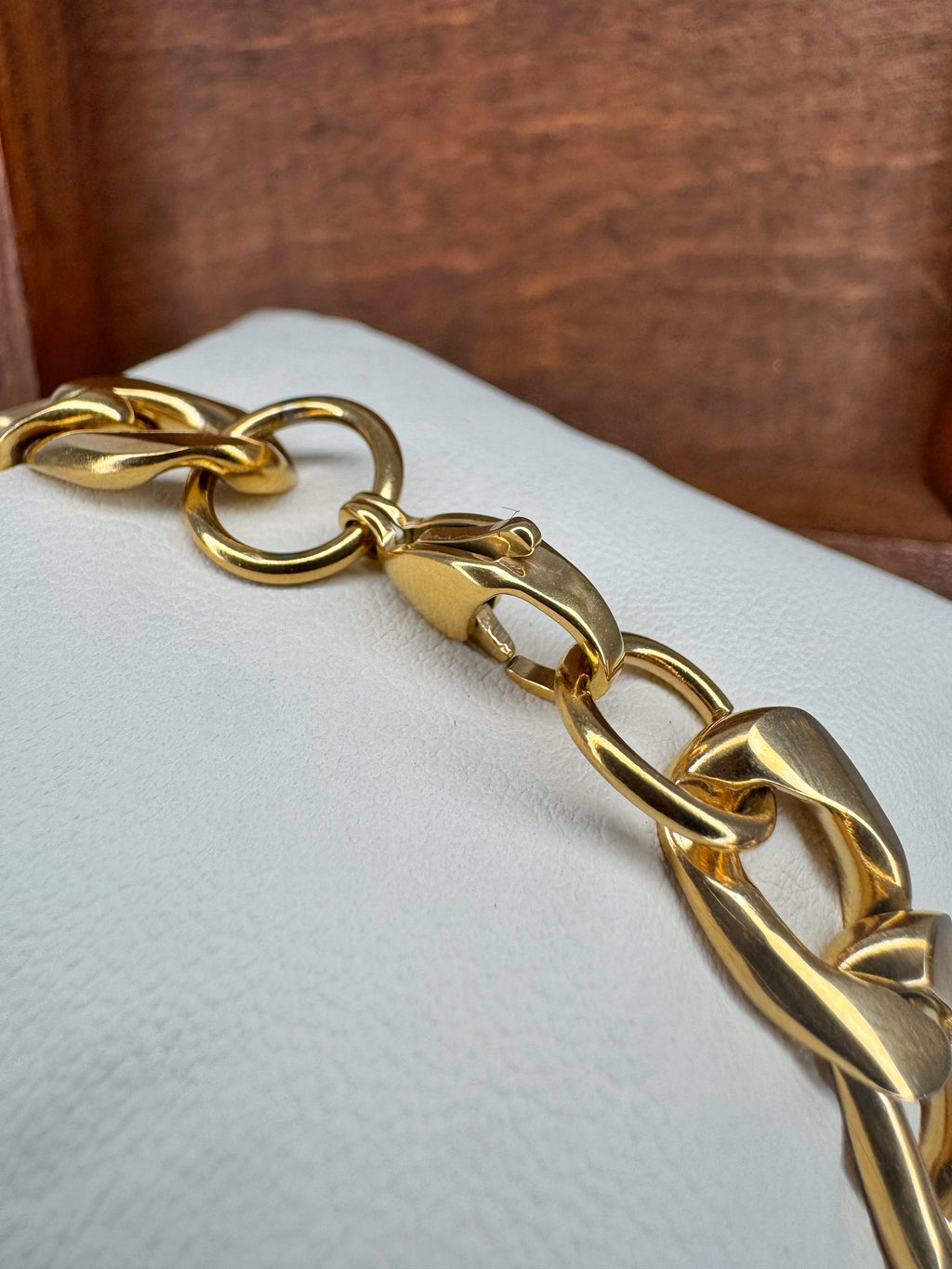 Gold chain bracelet on a white cushion with a wooden background