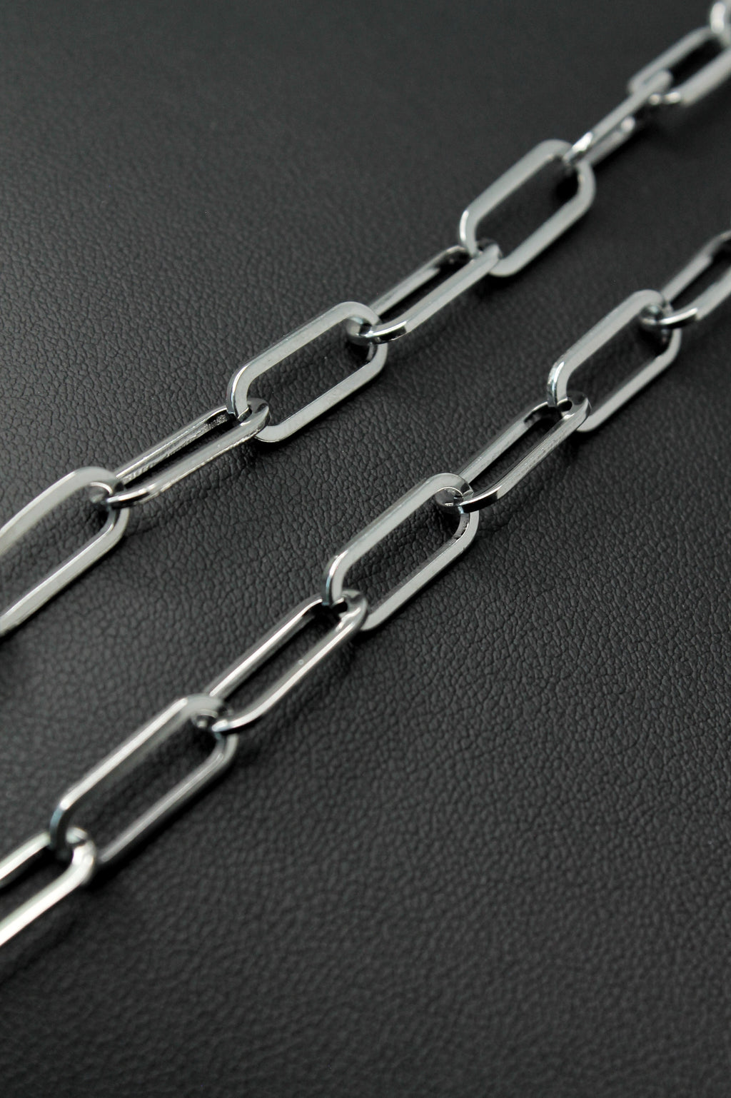 A close-up of a silver paperclip chain laid diagonally across a dark textured surface.
