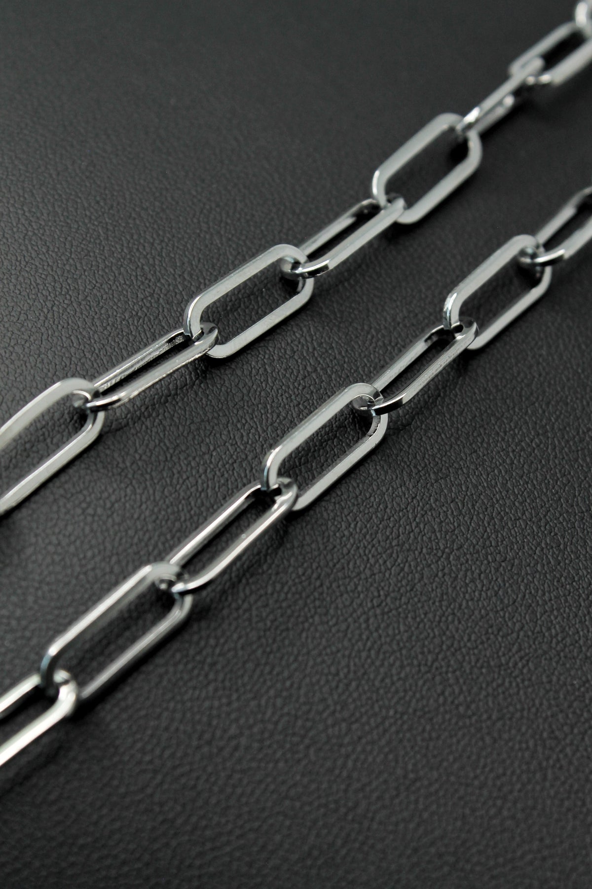 A close-up of a silver paperclip chain laid diagonally across a dark textured surface.