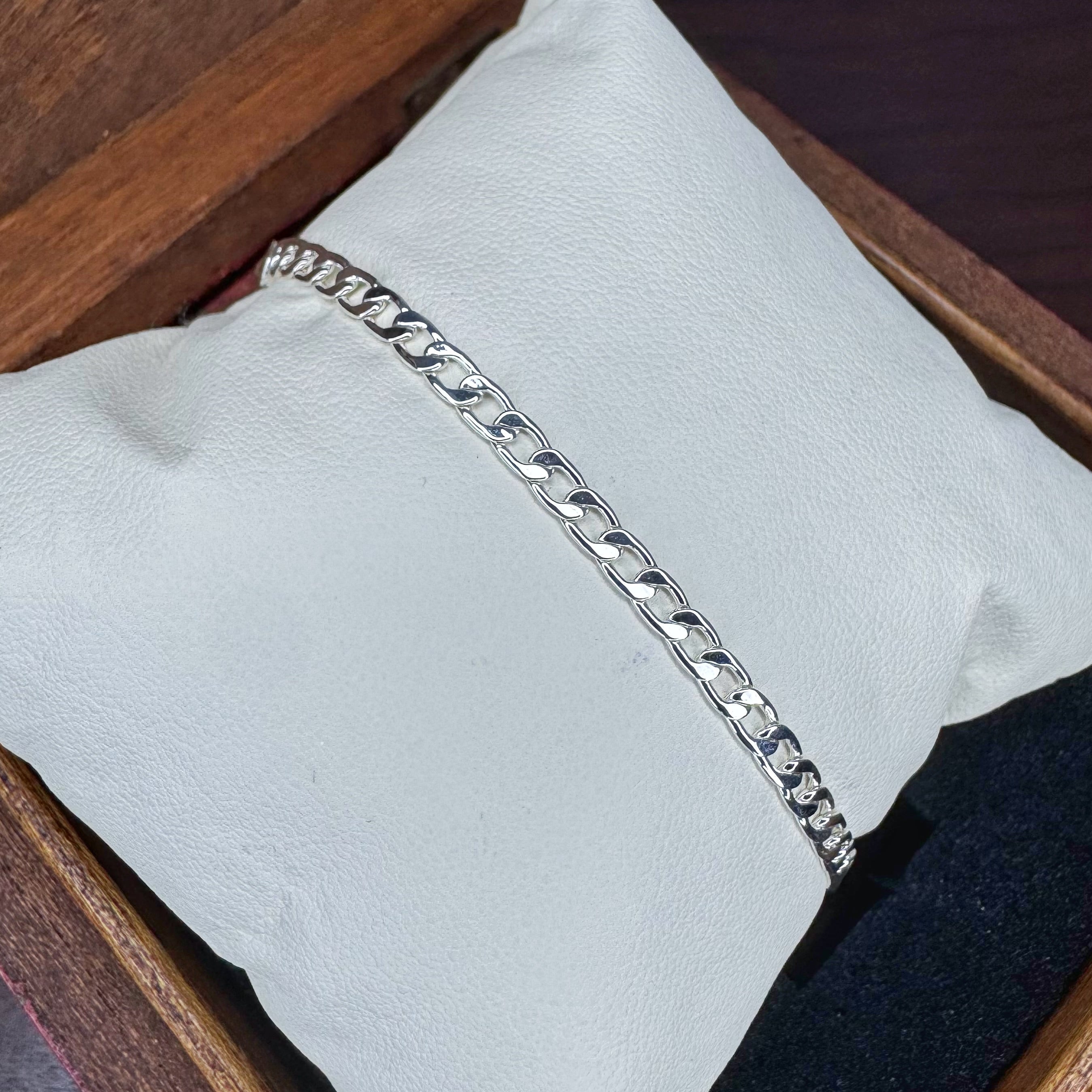 Silver chain bracelet on a light blue cushion with a wooden background