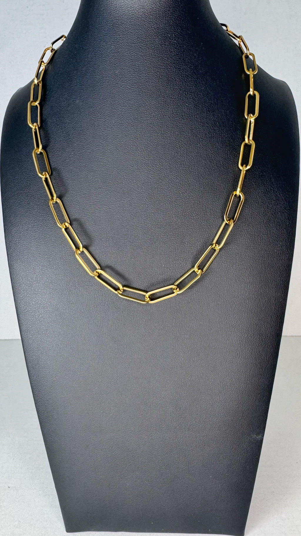 A gold-toned chain necklace with elongated rectangular links, displayed on a matte black jewelry bust against a light gray background.