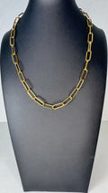 A gold-toned chain necklace with elongated rectangular links, displayed on a matte black jewelry bust against a light gray background.