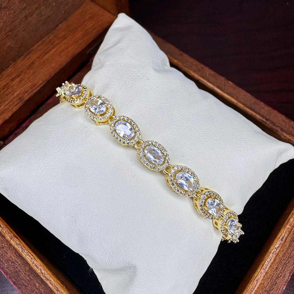 Gold bracelet with clear stones on a white cushion inside a wooden box