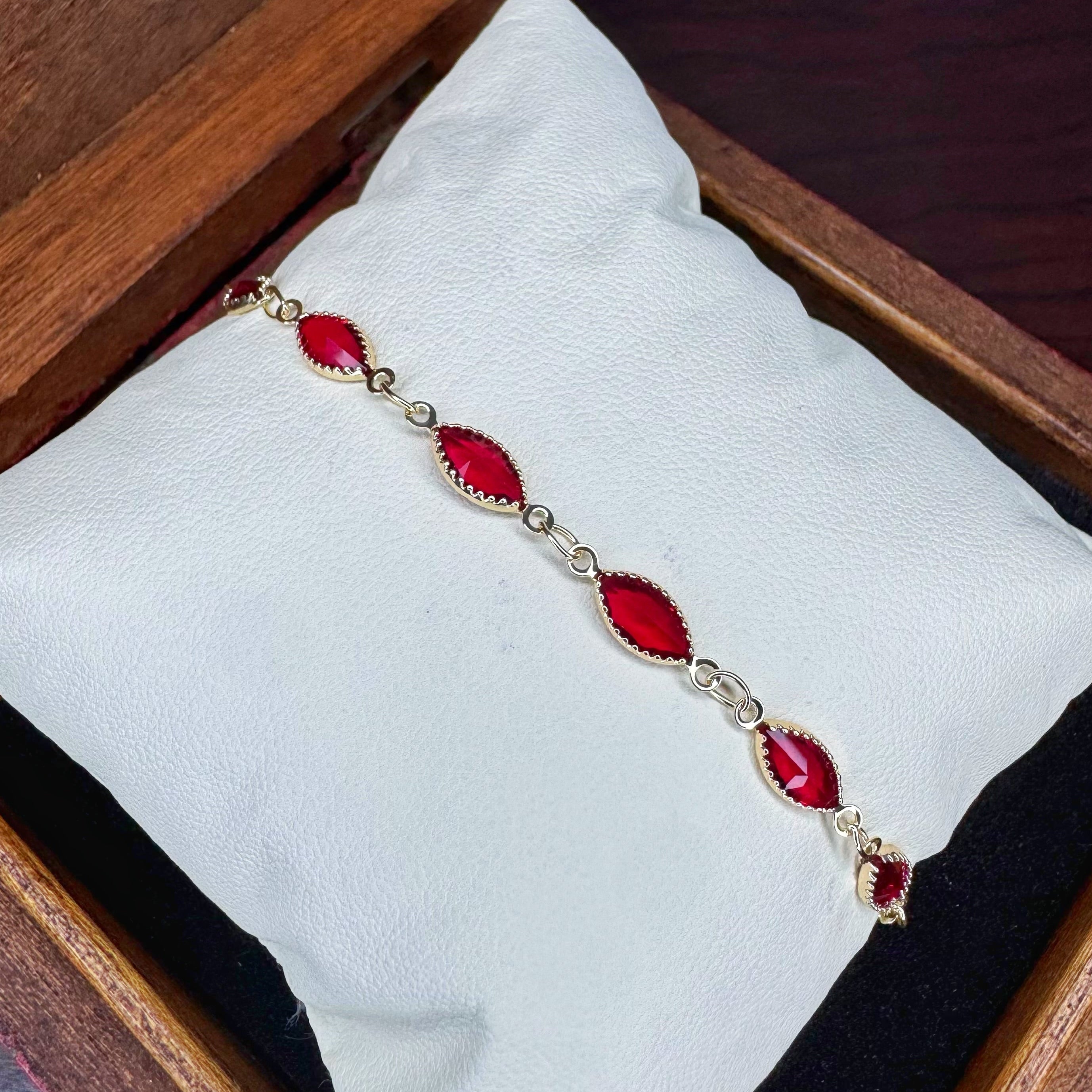 Bracelet with red gemstones on a white cloth inside a wooden box